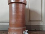 un grand pot marron posé par terre à côté d'un robinet