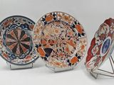 three decorative plates with designs on them sit on stands on a white surface