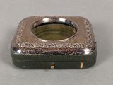 une petite boîte en argent avec un couvercle vert, posée sur une table