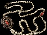 a white pearl necklace with a red stone and silver clasp
