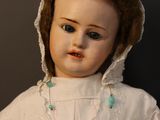 a close up of a doll wearing a white dress and a brown hat