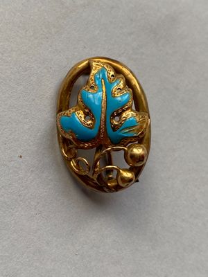 broche en or et turquoise ornée de feuilles sur un fond blanc