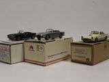 trois petites voitures posées sur des cartons, sur une surface blanche