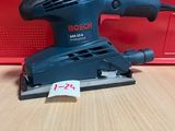 une ponceuse orbitale Bosch posée sur une table, à côté d'une boîte rouge