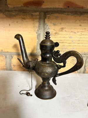 a small metal teapot sitting on a table next to a brick wall