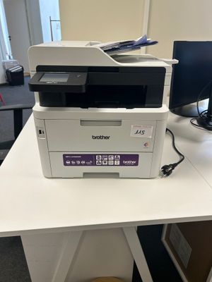a white printer sitting on top of a white desk next to a monitor