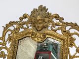 a mirror that has a gold frame with a face on it