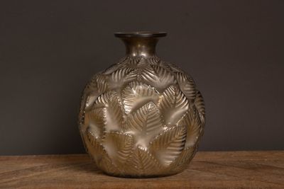 un vase en argent posé sur une table en bois, sur fond noir