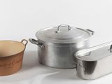 des casseroles et des poêles posées sur une surface blanche, avec une tasse devant elles