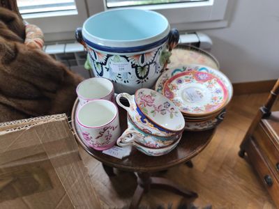 un chat assis sur une chaise à côté d'une table sur laquelle se trouvent des tasses et des soucoupes