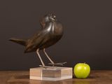 a bird statue sitting on top of a wooden block next to an apple