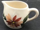 a white pitcher with a flower on it on a table