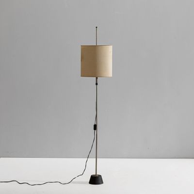 a black floor lamp with a beige shade on top of it