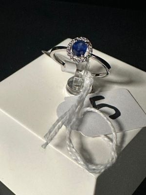 une boîte blanche sur laquelle est posée une bague sertie d'une pierre bleue