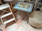 une petite table sur laquelle est posée une photo, avec un tabouret devant une bibliothèque
