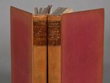 an old book with a red cover sitting on top of a table