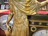 a gold statue of a man holding a book next to a clock