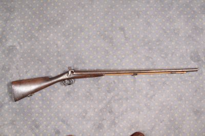 Une personne se tient debout à côté d'un fusil et d'un pistolet, sur un tapis