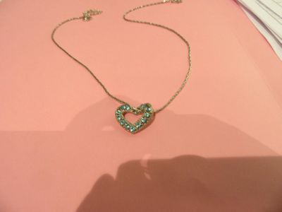 Collier Tiffany avec un cœur vert sur un fond rose, avec l'ombre de la main d'une personne