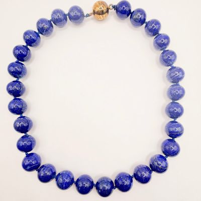 a close up of a necklace with blue beads on a white surface