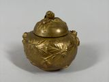 an image of a small gold pot with a lid on a white surface