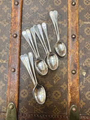 six cuillères en argent posées sur une vieille valise posée sur une table