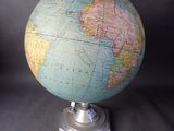 un petit globe terrestre posé sur un socle métallique, sur fond noir