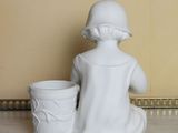 a statue of a girl sitting on the floor next to a cup