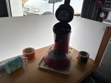 a red coffee maker sitting on a table next to a roll of toilet paper