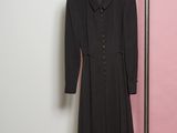 the black dress is hanging on a hanger in front of a pink wall