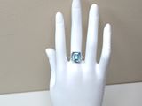 une main de mannequin blanche ornée d'une bague en topaze bleue