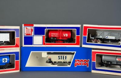 several model train cars in boxes on a gray surface