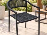 une chaise noire posée sur une terrasse, avec une table et des plantes en pot