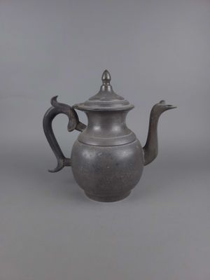 une vieille théière en argent avec une anse en métal sur fond gris