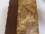 someone is holding a book with a brown cover on a white table