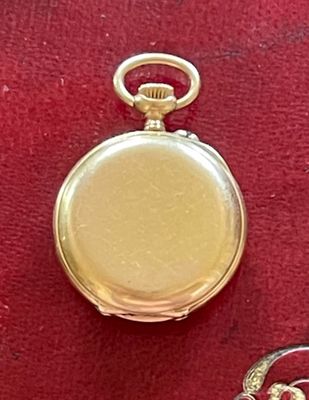 une montre de poche dorée, attachée à une chaîne posée sur un tissu rouge