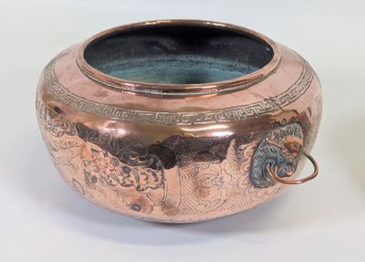 une grande casserole en cuivre avec une poignée, posée sur une table blanche