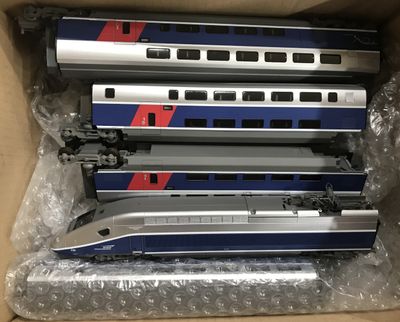 trois trains argentés et bleus se trouvent dans une boîte posée sur une table
