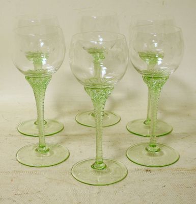 four green wine glasses sitting on top of a white table
