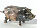 une petite figurine de cochon en métal posée sur une surface blanche