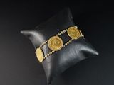 un gros plan sur un oreiller sur lequel est posé un bracelet composé de pièces d'or