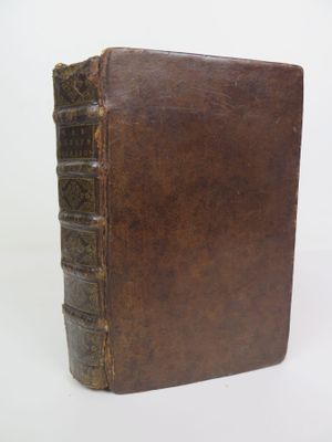 an old brown book sitting on top of a table next to a white wall