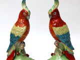 pair of red and green parrot figurines sitting on top of a green leaf