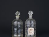 deux bouteilles en verre transparent avec des bouchons argentés, posées sur une surface noire