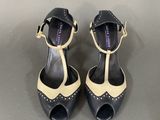 black and white high heeled shoes with gold accents on a grey surface