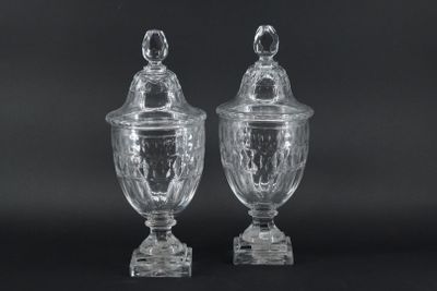 two clear glass vases with lids on a black background