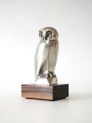 une image représentant une statue de chouette en argent posée sur un socle en bois