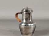une cafetière ancienne en argent, dotée d'une poignée en bois sur un fond gris