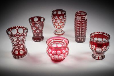 Plusieurs vases en verre rouge sont alignés sur une surface blanche