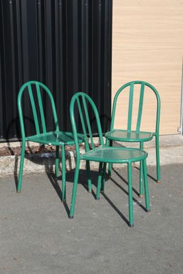three green chairs sitting next to each other in front of a building